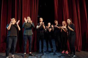 debout contre des rideaux rouges. groupe d'acteurs vêtus de vêtements de couleur sombre en répétition au théâtre photo