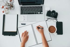 vue de dessus. jeune femme indépendante travaillant à l'intérieur du bureau pendant la journée. ordinateur portable et bloc-notes photo