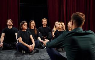 assis sur le sol. groupe d'acteurs vêtus de vêtements de couleur sombre en répétition au théâtre photo