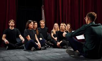 assis sur le sol. groupe d'acteurs vêtus de vêtements de couleur sombre en répétition au théâtre photo