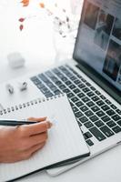 à l'aide d'un ordinateur portable et d'un bloc-notes. jeune femme indépendante travaillant à l'intérieur au bureau pendant la journée photo