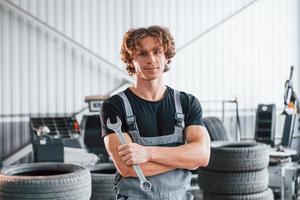 avec un outil à la main. homme adulte en uniforme de couleur grise travaille dans le salon de l'automobile photo