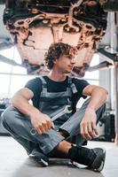 avec un outil à la main. homme adulte en uniforme de couleur grise travaille dans le salon de l'automobile photo