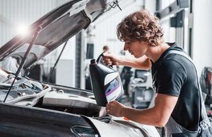 changement d'huile. homme adulte en uniforme de couleur grise travaille dans le salon de l'automobile photo