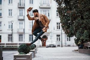 tient un chapeau et pose. jeune mannequin en vêtements à la mode est à l'extérieur de la ville pendant la journée photo