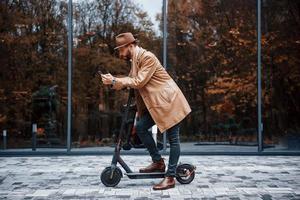 sur le scooter électrique. jeune mannequin en vêtements à la mode est à l'extérieur de la ville pendant la journée photo