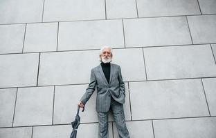 tient un parapluie. homme d'affaires senior en vêtements formels, aux cheveux gris et à la barbe est à l'extérieur photo