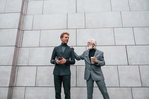 jeune homme avec un homme âgé dans des vêtements élégants est à l'extérieur ensemble. conception d'entreprise photo