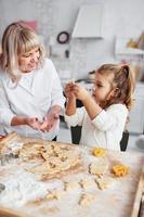 processus d'enseignement. grand-mère senior avec sa petite petite-fille prépare des bonbons pour noël dans la cuisine photo