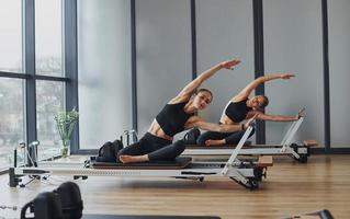 à l'aide d'équipements de gymnastique. deux femmes en tenue sportive et au corps mince ont ensemble une journée de yoga fitness à l'intérieur photo