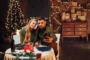 faire selfie en utilisant le téléphone. jeune couple charmant dîner ensemble à l'intérieur photo