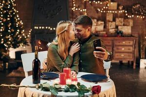 faire selfie en utilisant le téléphone. jeune couple charmant dîner ensemble à l'intérieur photo