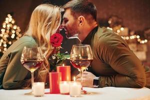 tenant une belle rose rouge. jeune couple charmant dîner ensemble à l'intérieur photo