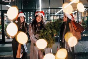 détient le sapin. trois femmes joyeuses passent les vacances de noël ensemble à l'extérieur. conception du nouvel an photo