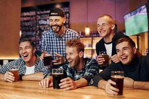 les fans de football regardent la télévision. groupe de personnes ensemble à l'intérieur dans le pub s'amuser le week-end photo