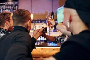 acclamant en frappant des verres à bière. groupe de personnes ensemble à l'intérieur dans le pub s'amuser le week-end photo