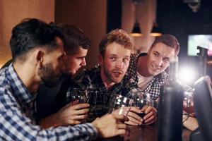 acclamant en frappant des verres à bière. groupe de personnes ensemble à l'intérieur dans le pub s'amuser le week-end photo