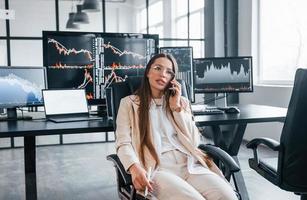 parle par téléphone. la jeune femme courtière travaille à l'intérieur au bureau. beaucoup d'affichages photo