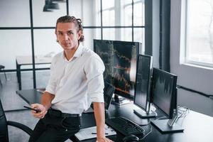 le jeune agent de change masculin travaille à l'intérieur au bureau. beaucoup d'affichages photo