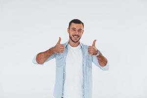 pouces vers le haut. jeune bel homme debout à l'intérieur sur fond blanc photo