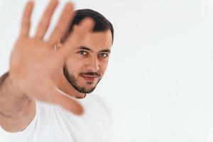 geste d'arrêt. jeune bel homme debout à l'intérieur sur fond blanc photo