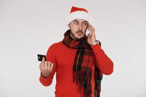 avec téléphone et carte de crédit. jeune bel homme en vêtements de nouvel an debout à l'intérieur sur fond blanc photo