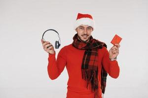 écouteurs et boîte-cadeau rouge. jeune bel homme en vêtements de nouvel an debout à l'intérieur sur fond blanc photo