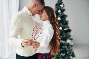 tient des bonbons dans les mains. jeune couple romantique célèbre le nouvel an ensemble à l'intérieur photo