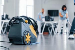 femme utilise un aspirateur. un groupe de travailleurs nettoie un bureau moderne ensemble pendant la journée photo