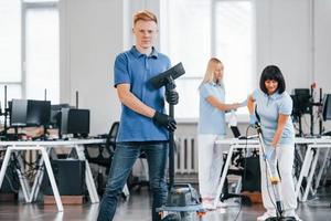 gars avec aspirateur. un groupe de travailleurs nettoie un bureau moderne ensemble pendant la journée photo