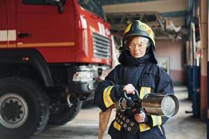 tuyau dans les mains. femme pompier en uniforme de protection debout près du camion photo