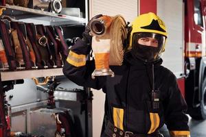 tient le tuyau. pompier masculin en uniforme de protection debout près du camion photo