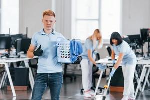 l'homme tient le panier. un groupe de travailleurs nettoie un bureau moderne ensemble pendant la journée photo