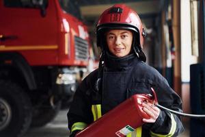 tient l'extincteur dans les mains. femme pompier en uniforme de protection debout près du camion photo