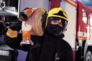 tient le tuyau. pompier masculin en uniforme de protection debout près du camion photo