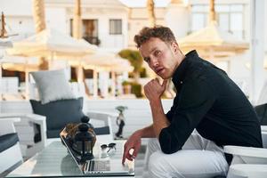 est assis près de la table. jeune homme est à l'extérieur pendant la journée ensoleillée. notion de vacances photo