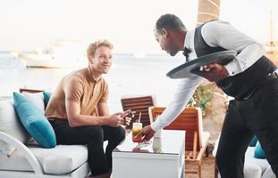 servi par un serveur. jeune homme est à l'extérieur pendant la journée ensoleillée. notion de vacances photo