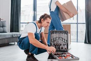 utilise des outils de cas. deux jeunes déménageurs en uniforme bleu travaillant à l'intérieur dans la chambre photo