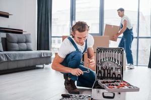 mallette avec équipement. deux jeunes déménageurs en uniforme bleu travaillant à l'intérieur dans la chambre photo