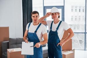 document à signer. deux jeunes déménageurs en uniforme bleu travaillant à l'intérieur dans la chambre photo