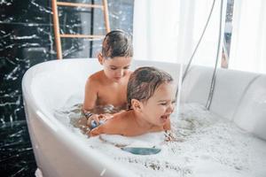 deux enfants s'amusant et se lavant dans le bain à la maison. entraider photo