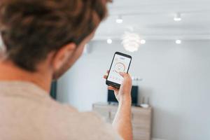 tient le téléphone. vue arrière d'un homme adulte qui contrôle à l'intérieur la technologie de la maison intelligente photo