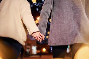 se tenant par la main. heureux jeune couple célébrant le nouvel an à l'extérieur dans la rue photo