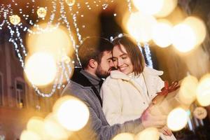 femme tient une boîte-cadeau. heureux jeune couple célébrant le nouvel an à l'extérieur dans la rue photo