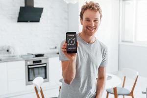 un jeune homme en vêtements décontractés contrôle à l'intérieur la technologie de la maison intelligente photo