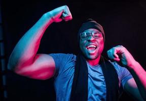 en bonnet et écharpe. éclairage néon futuriste. jeune homme afro-américain dans le studio photo