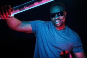 avec des lunettes de soleil. éclairage néon futuriste. jeune homme afro-américain dans le studio photo