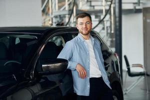 homme qui a réussi dans des verres debout près d'une voiture neuve à l'intérieur photo