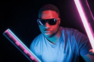 avec des lunettes de soleil. éclairage néon futuriste. jeune homme afro-américain dans le studio photo