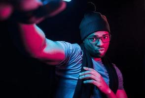 en bonnet et écharpe. éclairage néon futuriste. jeune homme afro-américain dans le studio photo